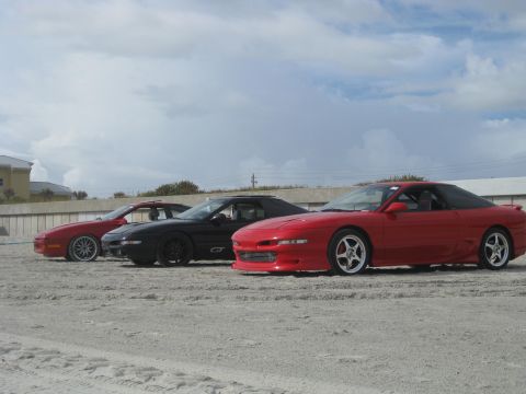 1994 Ford Probe - Three Ford Probes are parked in a line on a sandy beach under a cloudy sky.