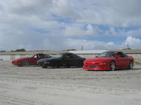 1994 Ford Probe - Three 1994 Ford Probe cars are parked side-by-side on a sandy surface under a cloudy sky.