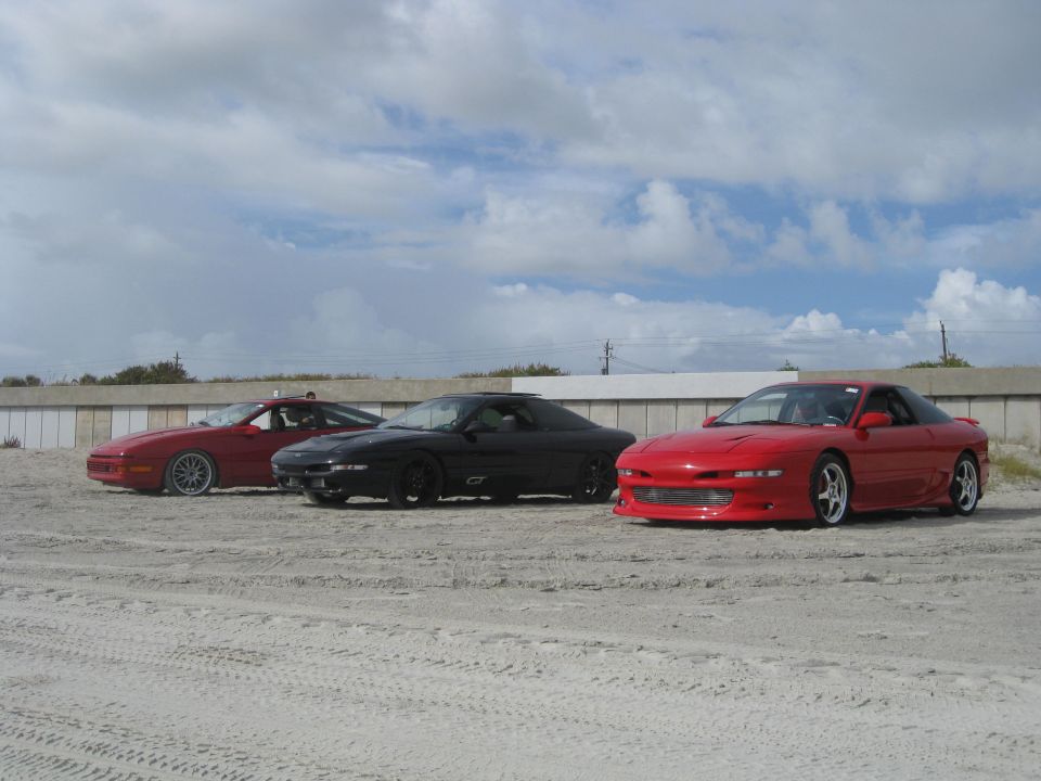 Three 1994 Ford Probe cars parked on sand with a cloudy sky