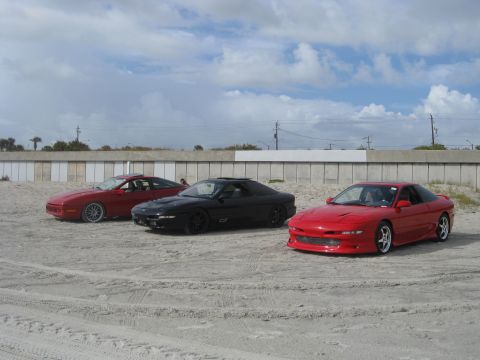 1994 Ford Probe - Three Ford Probes are lined up on a sandy lot near a wall under a cloudy sky.