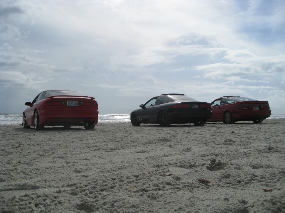 Three coupes parked on a sandy beach with the ocean in the background