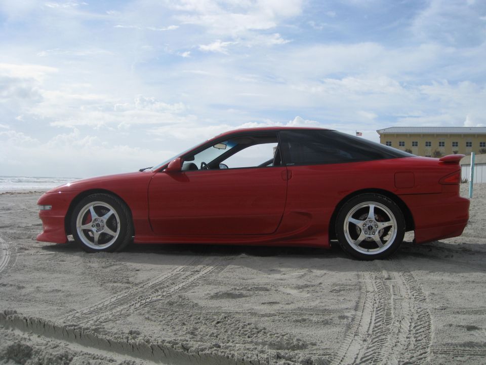 Red coupe with black roof and spoiler parked on a sandy beach with tire tracks