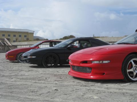 1994 Ford Probe - Three 1994 Ford Probes are lined up on a sandy beach under a cloudy sky.