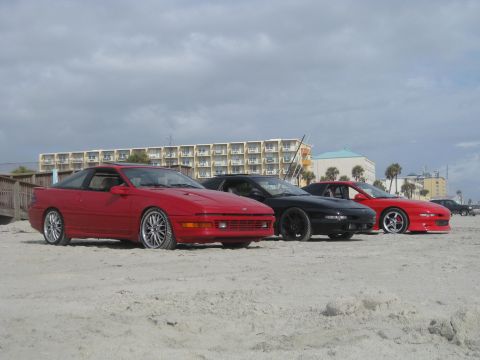 1994 Ford Probe - Three Ford Probes lined up on the sand near the ocean with a hotel and palm trees behind them.