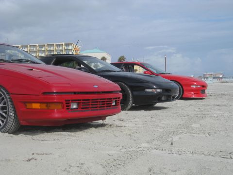 1994 Ford Probe - Three 1994 Ford Probes lined up on the beach under a cloudy sky.