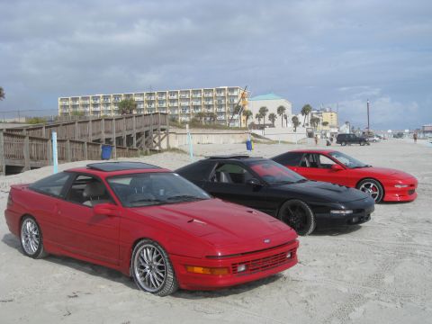 1994 Ford Probe - Three Ford Probe cars are parked on the sand near a boardwalk and hotel.
