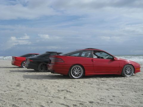 1994 Ford Probe - Three coupes are parked on the beach with the ocean in the background.
