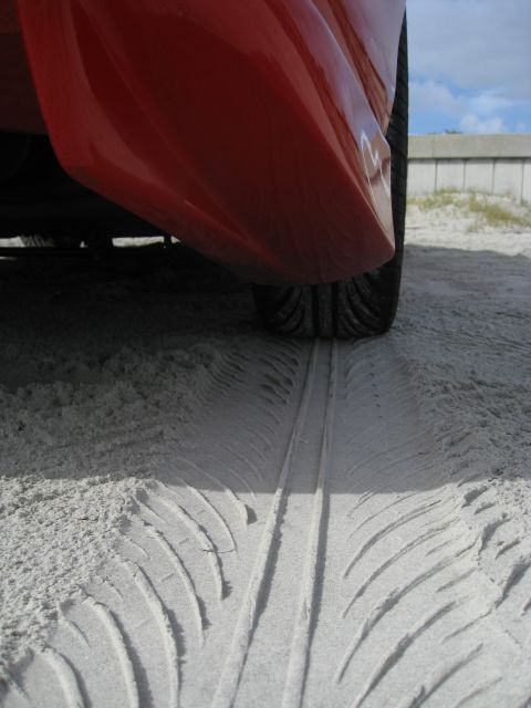 1994 Ford Probe - A vehicle's tire has left distinct tracks in the sand, suggesting it drove on a beach or sandy area.