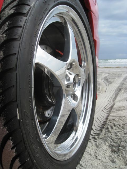 1994 Ford Probe - A close-up of a car's wheel and tire on a beach, with tire tracks visible in the sand.