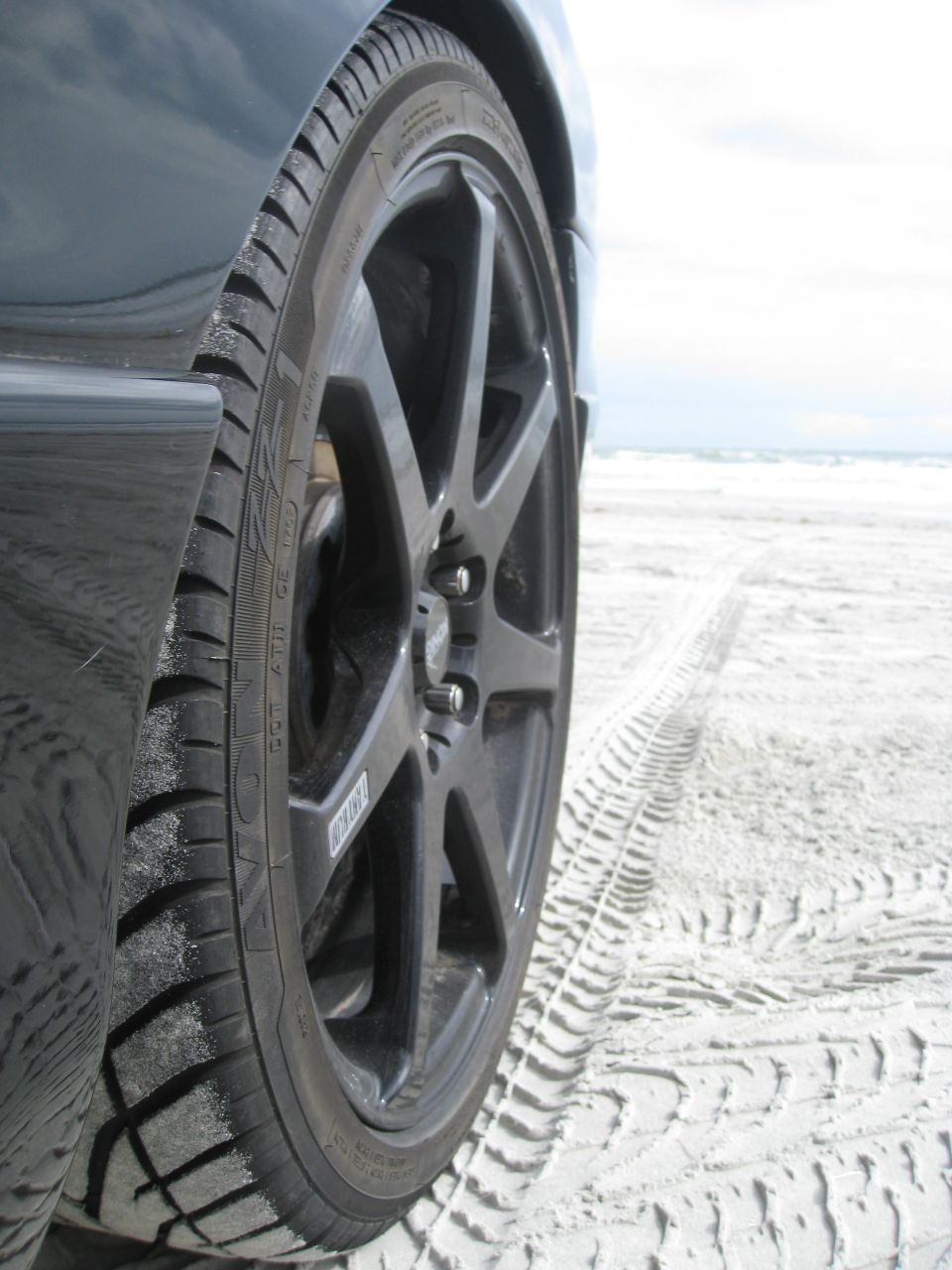Black car wheel on beach with tire tracks