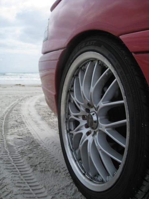 1994 Ford Probe - Custom wheels on a red car at the beach, with tire tracks in the sand.
