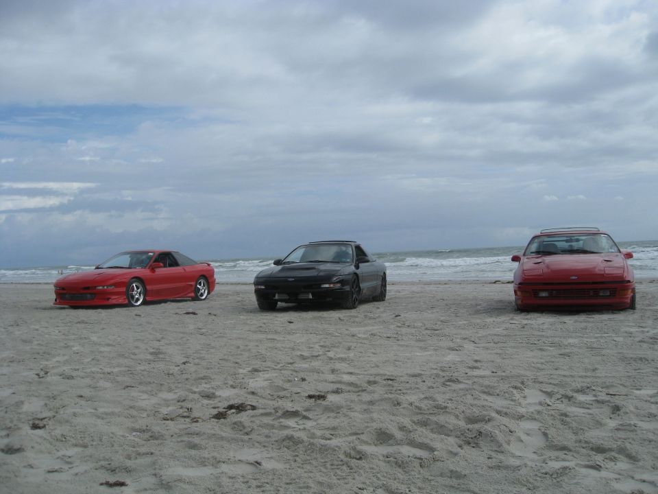Three sports coupes parked on a sandy beach with the ocean in the background