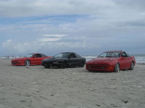 1994 Ford Probe - Three Ford Probe cars are parked on the sand near the ocean under a cloudy sky.