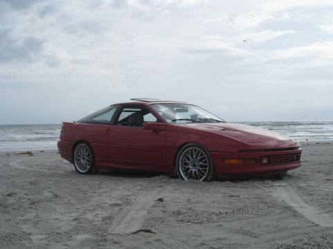 1994 Ford Probe - This red 1994 Ford Probe is parked on the sand near the ocean waves.