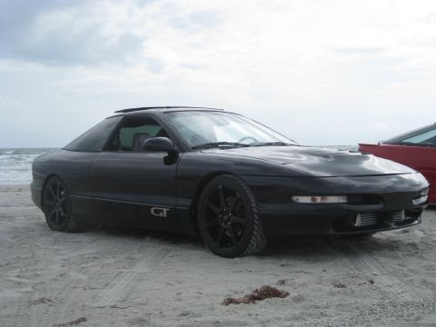1994 Ford Probe - A black Ford Probe GT sits on the sand near the ocean, with a portion of a red car visible on the right.