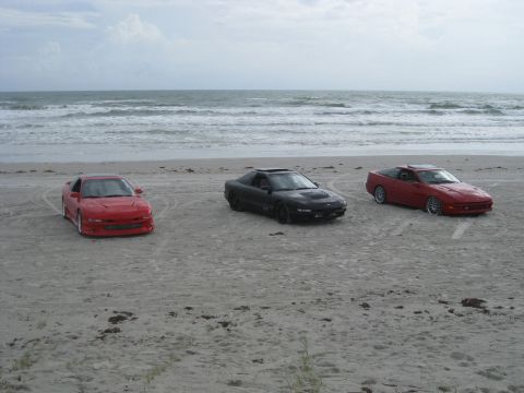 1994 Ford Probe - Three sports cars are parked on a sandy beach with the ocean waves in the background.