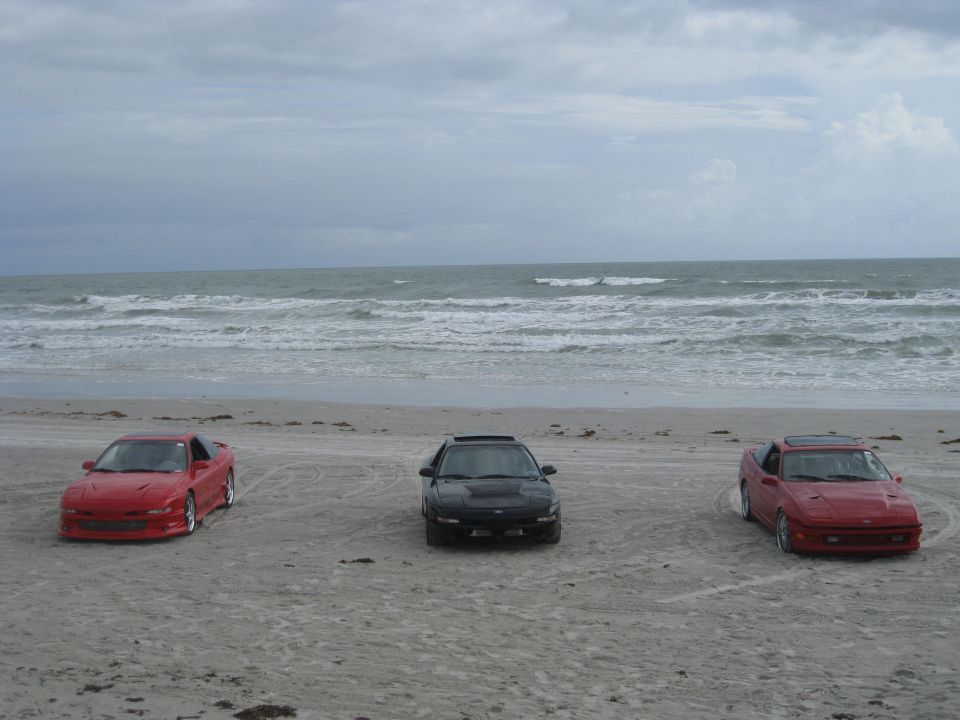 Three sports cars parked on a sandy beach with the ocean in the background