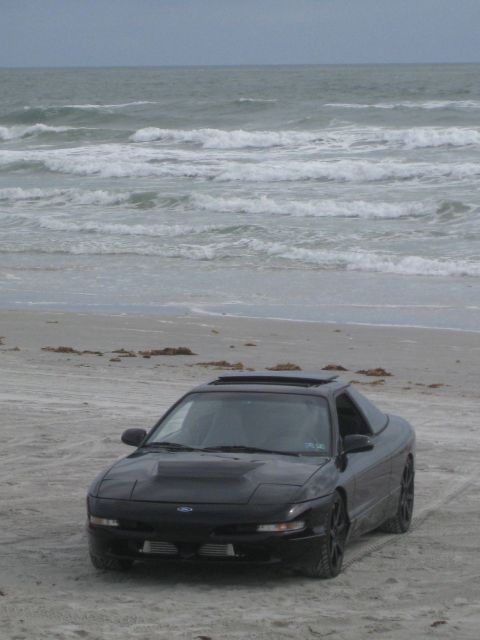 1994 Ford Probe - A black 1994 Ford Probe is parked on a beach with the ocean in the background.
