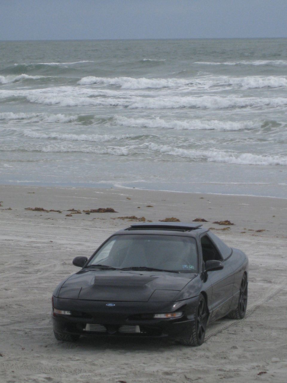 Black 1994 Ford Probe on a sandy beach with ocean waves