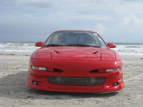 1994 Ford Probe - A red 1994 Ford Probe is parked on a sandy beach with the ocean in the background.