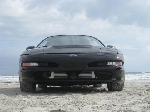 1994 Ford Probe - A black 1994 Ford Probe sits on the sand near the ocean under a cloudy sky.