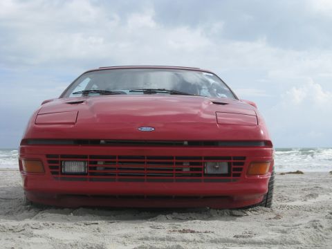 1994 Ford Probe - A red car with pop-up headlights sits on a sandy beach with the ocean in the background.
