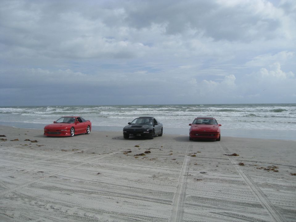 Three sports cars parked on a sandy beach with the ocean and cloudy sky in the background