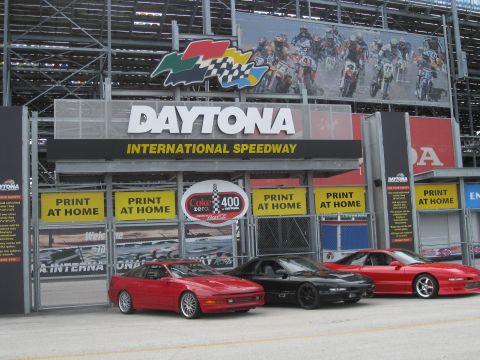 1994 Ford Probe - Three sports cars are parked in front of the Daytona International Speedway, with a large billboard motocross riders above.