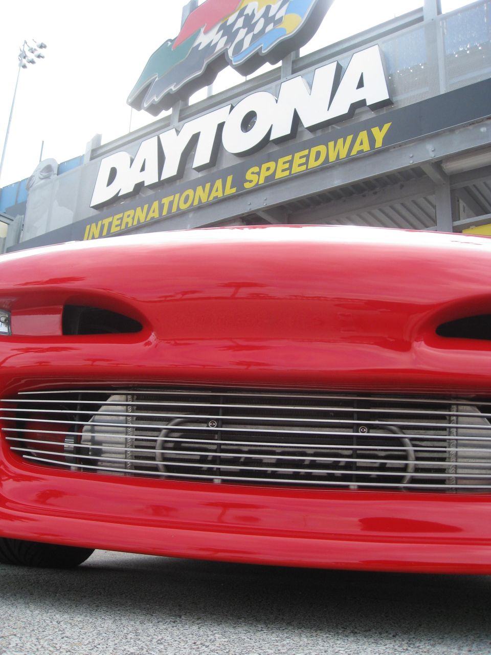 Red car front end with chrome grille, Daytona International Speedway sign in background