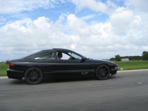1994 Ford Probe - A black 1994 Ford Probe GT is captured in motion on a highway under a cloudy sky.