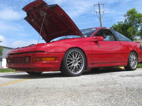 1994 Ford Probe - A red coupe with its hood open sits parked on a paved surface under a cloudy sky.