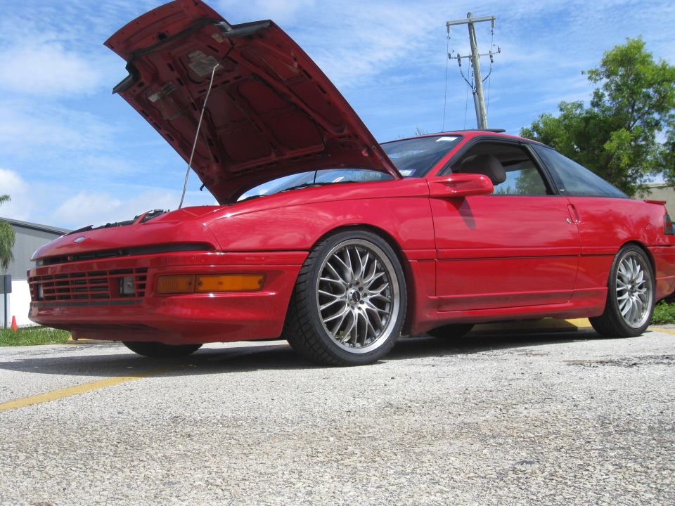red coupe with hood open, aftermarket wheels, parked outside