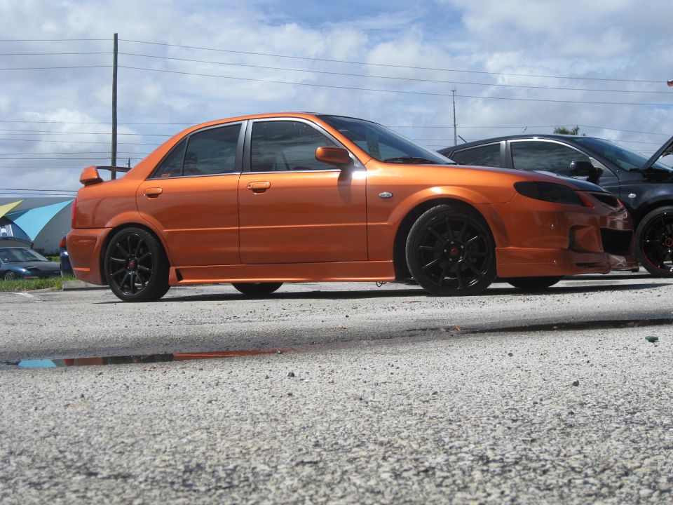Orange sedan with black wheels and a spoiler parked next to a black car
