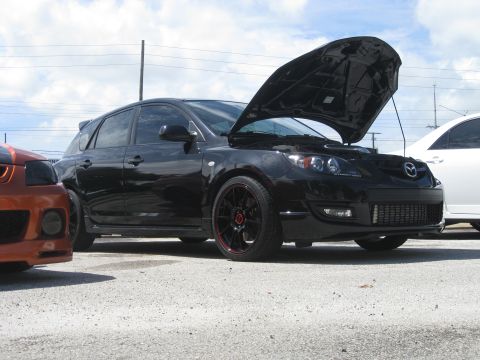 1994 Ford Probe - A black Mazda 3 hatchback is parked with its hood open, next to another vehicle.