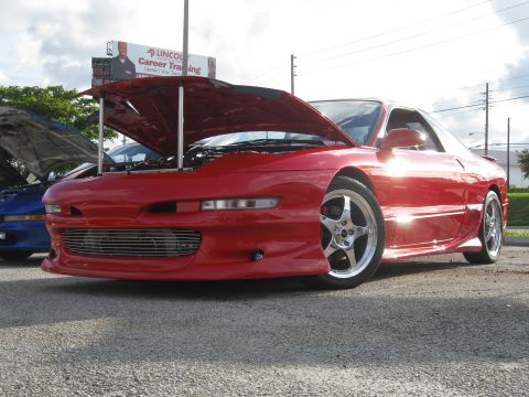 1994 Ford Probe - A red sports coupe is parked with its hood open, alongside another vehicle, under a cloudy sky.