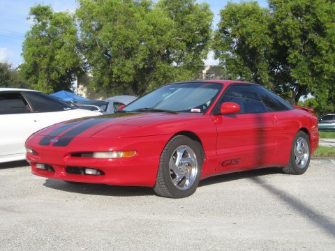 1994 Ford Probe - A red 1994 Ford Probe with racing stripes is parked outside on a sunny day.