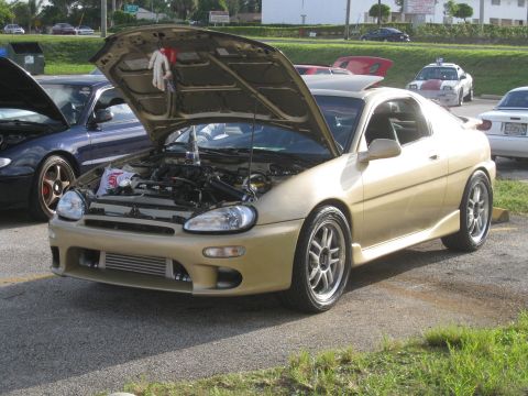 1994 Ford Probe - A gold coupe is displayed with its hood open, revealing the engine bay and an aftermarket intercooler.