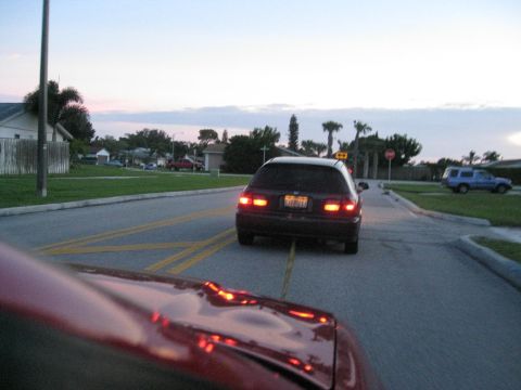 1994 Ford Probe - A dark hatchback is seen from behind driving down a residential street as the sun sets.