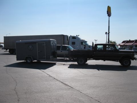 1977 Ford F-250 - A 1977 Ford F-250 crew cab flatbed truck is seen towing a trailer, with other trucks in the background.