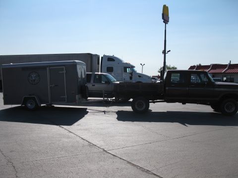 1977 Ford F-250 - A Ford pickup truck tows a cargo trailer past a semi-truck and a fast-food restaurant.