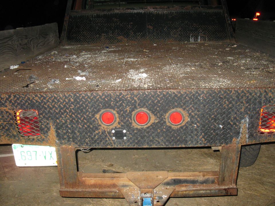 Rear of a flatbed truck with three red taillights and a license plate reading 697 VX