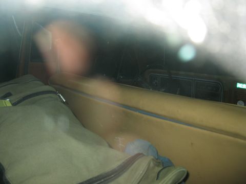1977 Ford F-250 - The interior of a vehicle shows bags on the seat and a blurry figure in the background.