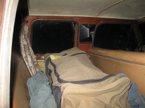 1977 Ford F-250 - The interior of a truck cab shows tan seats and luggage, with a camouflage fabric hanging near the window.