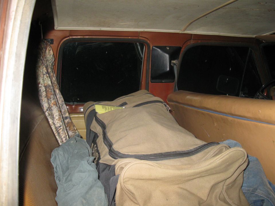 Interior of a brown truck cab with tan seats, camouflage fabric, and duffel bags. A yellow tag is visible on a bag