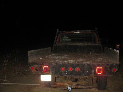 1977 Ford F-250 - The back of a flatbed truck is shown at night, with its brake lights illuminated.