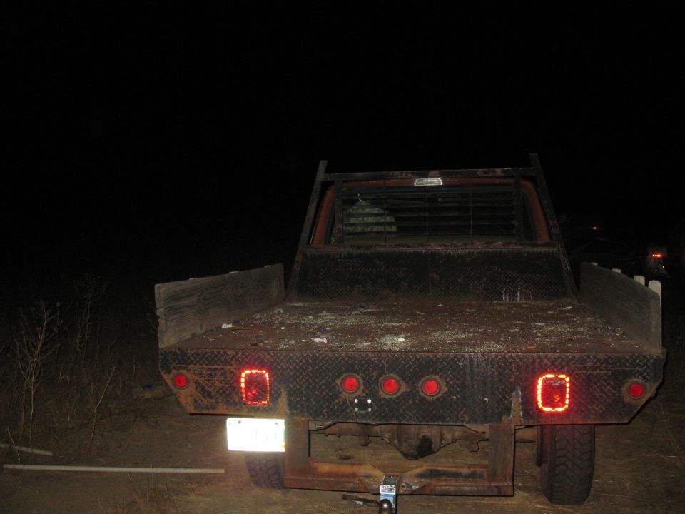 Rear view of a flatbed truck at night. It has diamond plate on the bed and multiple red taillights