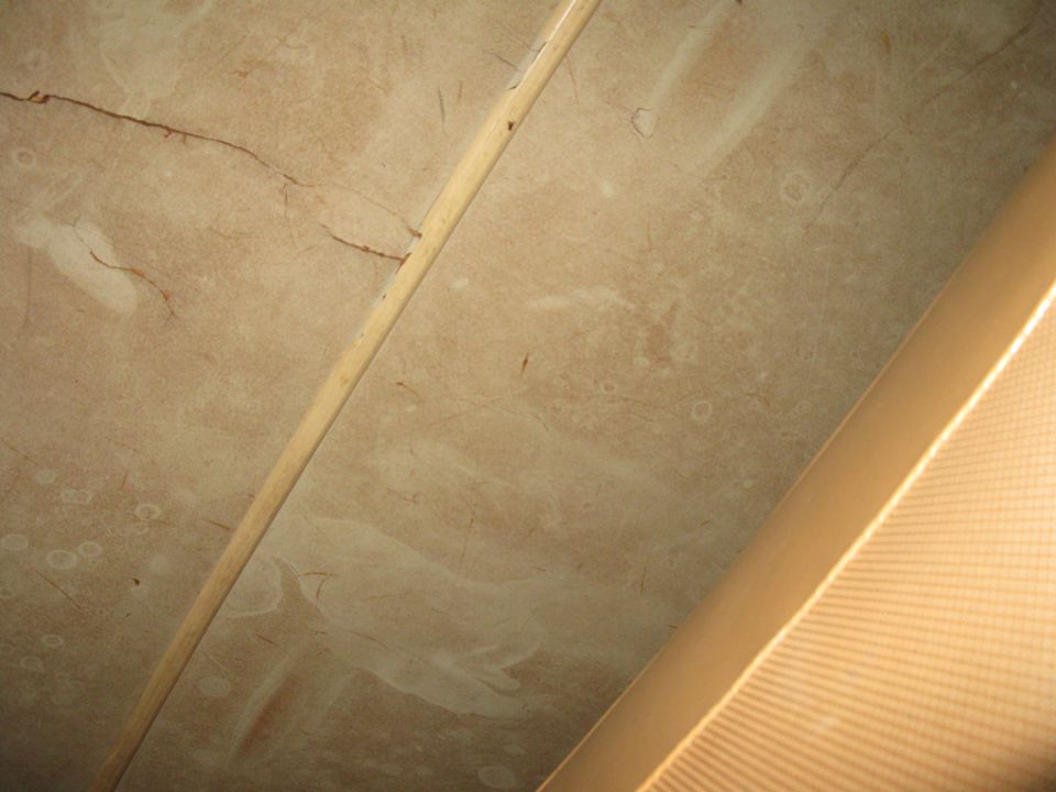 Close-up of a cracked, tan headliner with a wooden trim piece