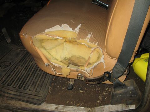 1977 Ford F-250 - The interior of a vehicle shows a heavily damaged tan seat with torn upholstery, revealing yellow foam padding underneath.