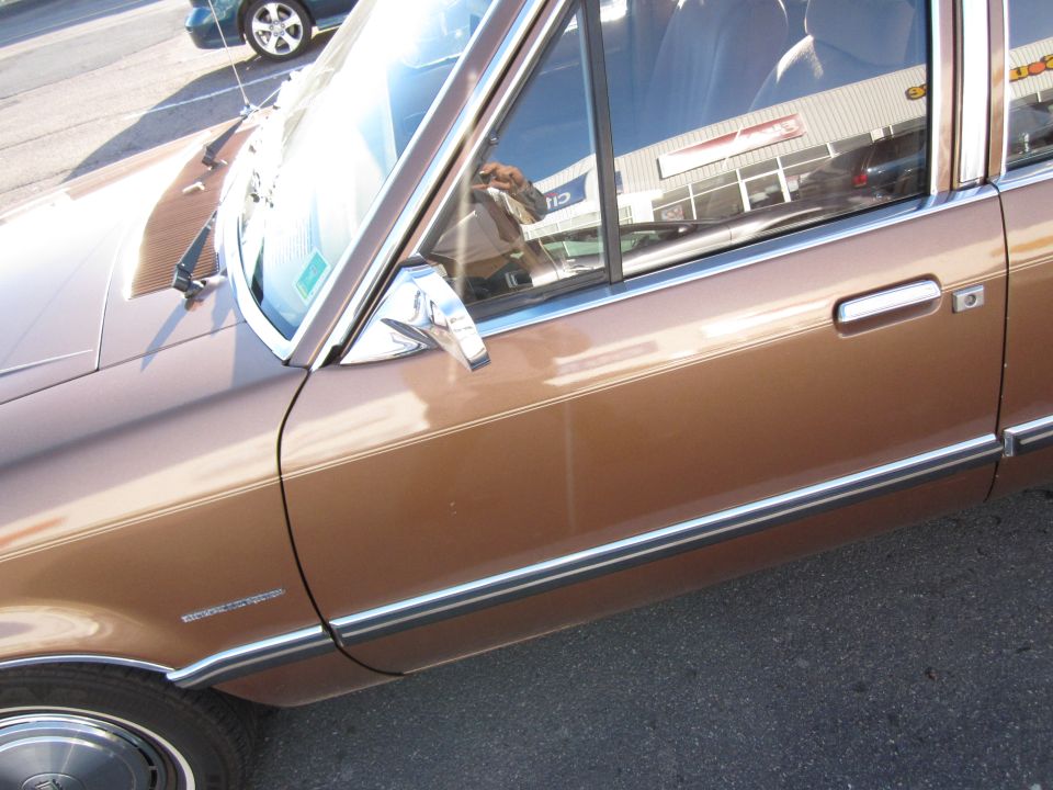 Side view of a brown sedan with chrome trim and a reflection of a building in the window