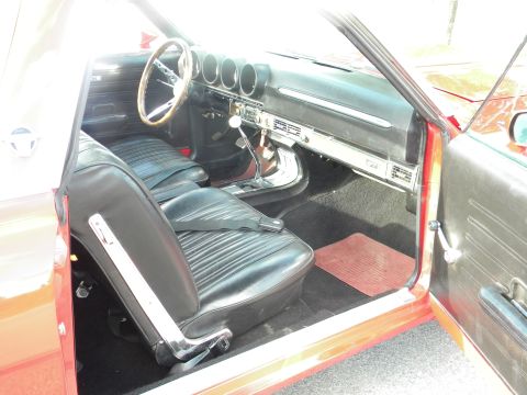 1979 Ford F-250 - The interior of a red car features black vinyl seats, a wooden steering wheel, and a dashboard with multiple gauges.